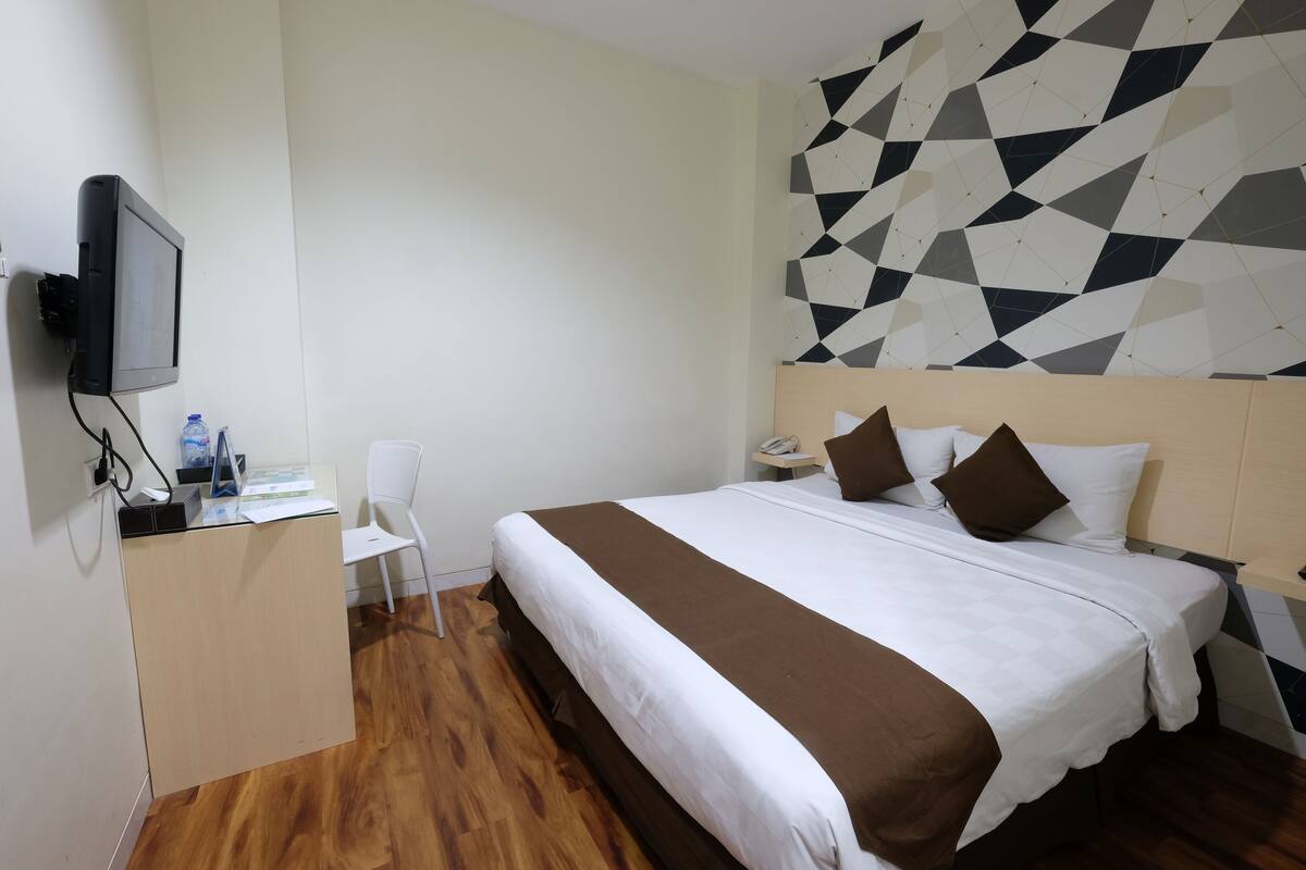 Une chambre d’hôtel avec un lit, un bureau équipé d’un ordinateur, une chaise et un mur orné d’un motif géométrique.