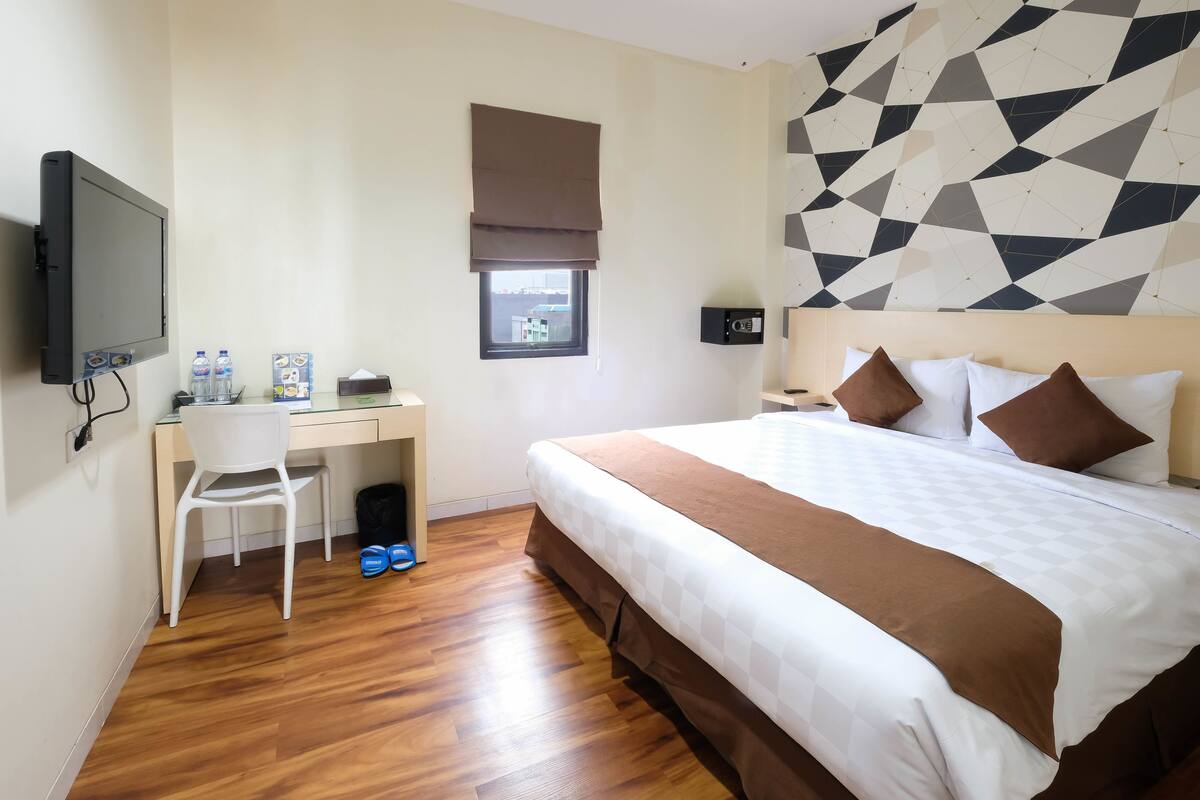 Une chambre d’hôtel équipée d’un lit, d’un bureau, d’une chaise, d’une télévision et d’une fenêtre donnant sur un paysage agréable.