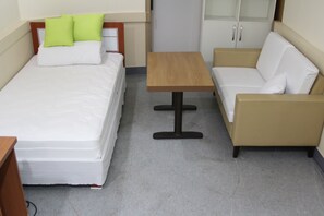 A small, neatly arranged room with a bed, a sofa, a small table, and a cabinet.