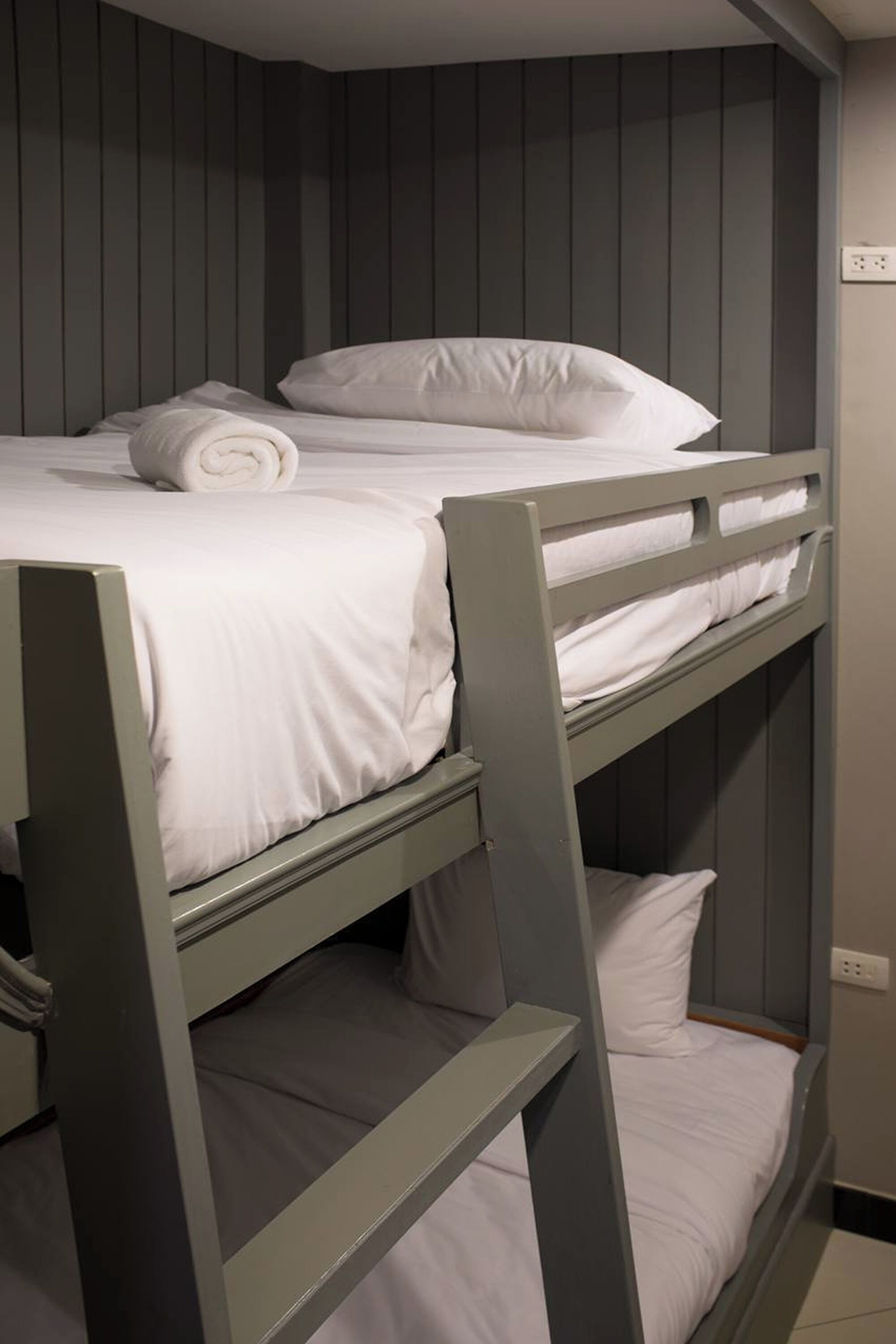 A bunk bed with white bedding and a rolled towel on the top bunk.