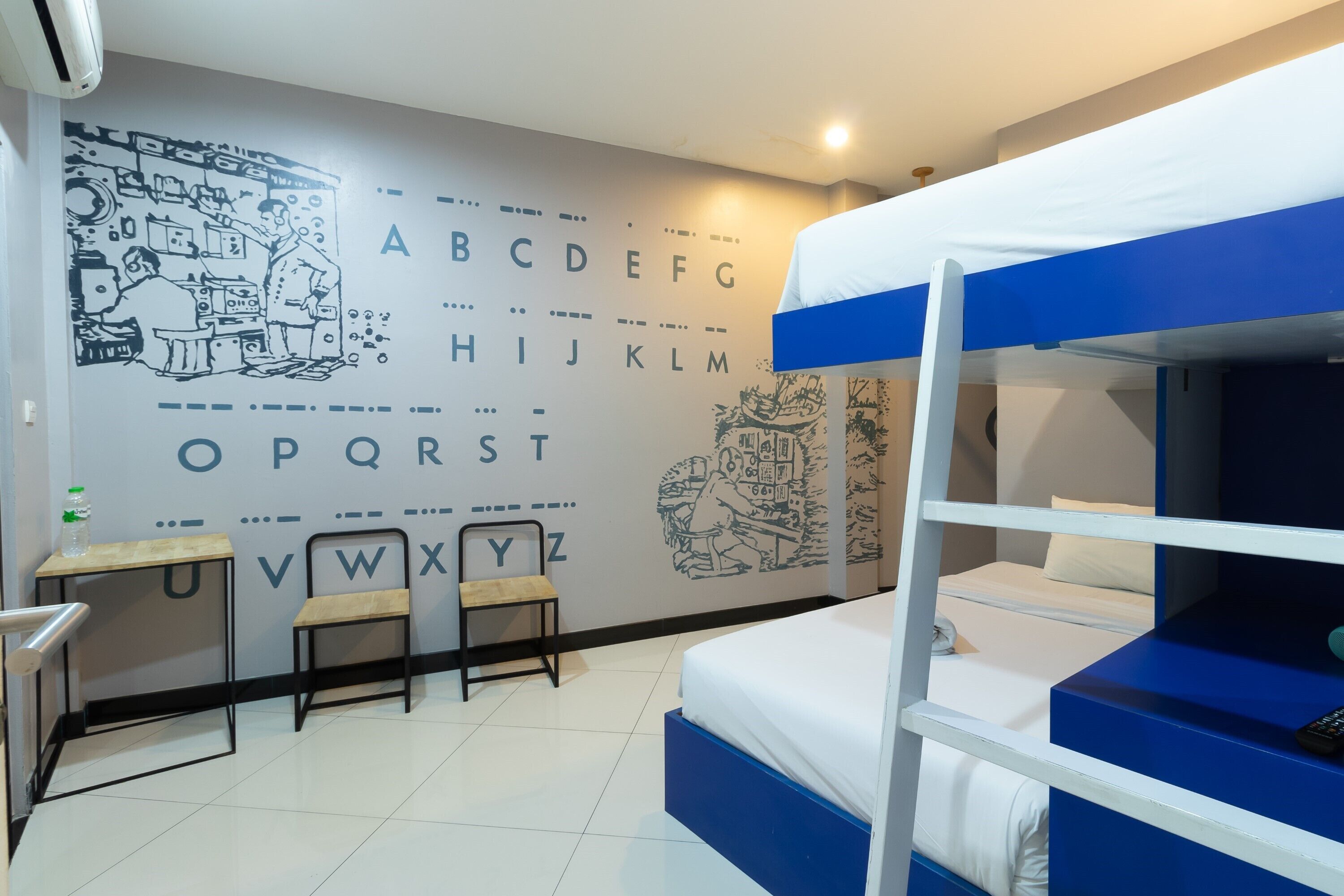 A bunk bed room with a desk and chair, a wall with alphabet letters and a ship illustration, and a window with a view of a building.