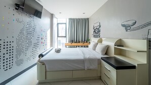 Quarto moderno com cama, mesa de cabeceira e televisão presa na parede.