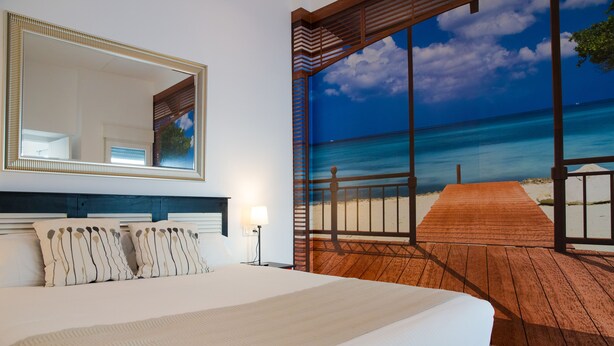 A bedroom with a large bed, a mirror, and a view of a beach through a large window. - Holidays2Malaga Comfort Apartments (Málaga)