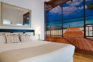 A bedroom with a large bed, a mirror, and a view of a beach through a large window.