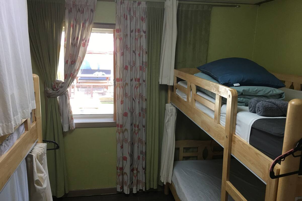 Een slaapkamer met een stapelbed, een raam, gordijnen en uitzicht op een buitenruimte.