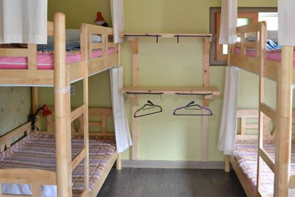 Een slaapkamer met een stapelbed van hout, een tafeltje en een wandrek om was te drogen.