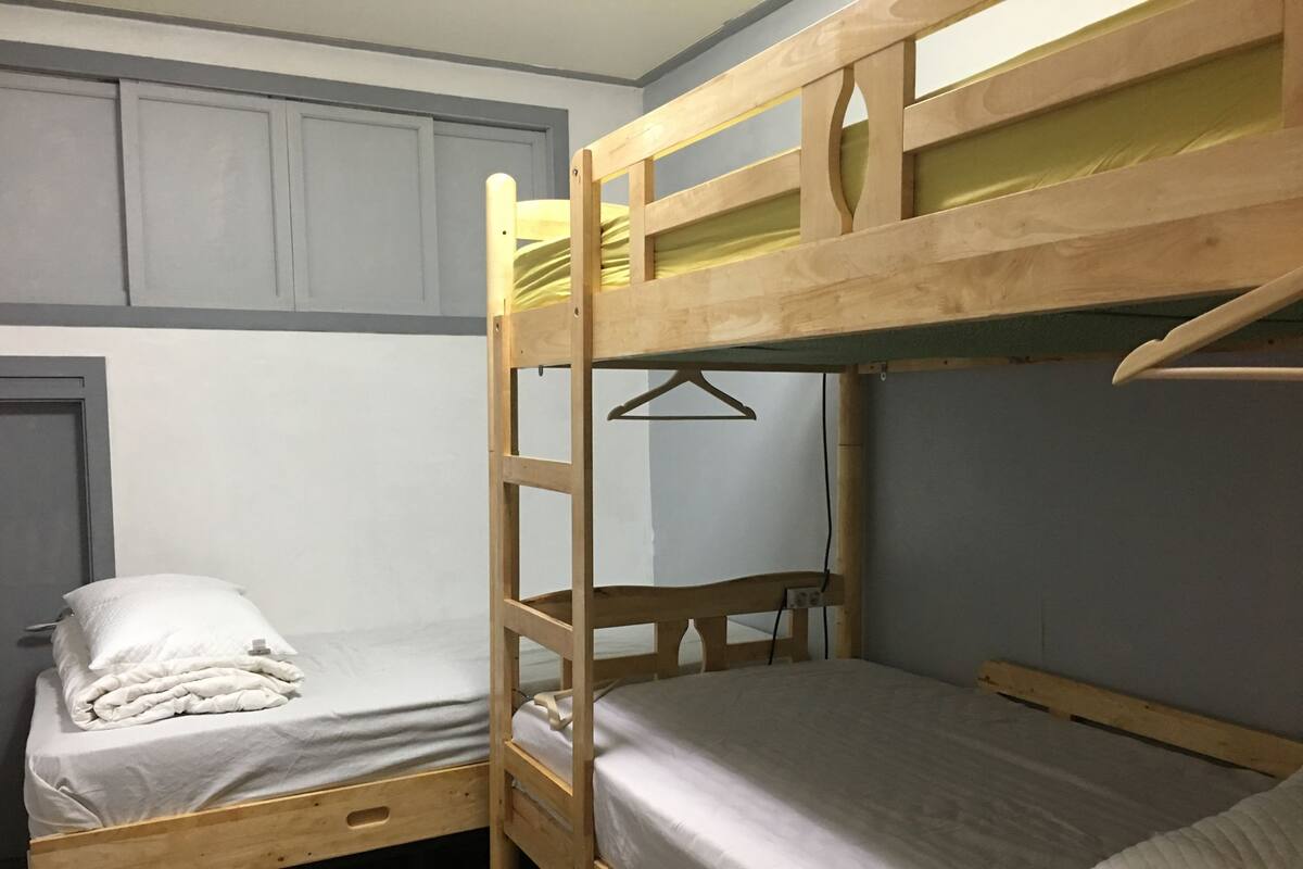 Een slaapkamer met een tweepersoons stapelbed en een enkel bed, beide van hout.