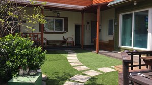 Een patio met een houten terras, een groen kunstgrasveld en een pad van stenen.