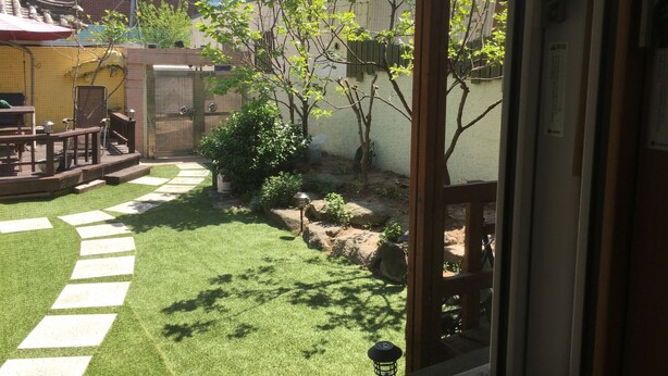 Uitzicht op een binnenplaats met een houten terras, een kleine tuin en een poort naar een gebouw.