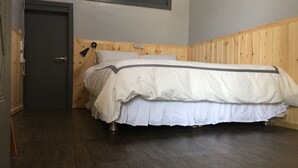 Een slaapkamer met een houten hoofdbord, een bed met wit beddengoed, een donkere houten vloer en een deur met een handvat.