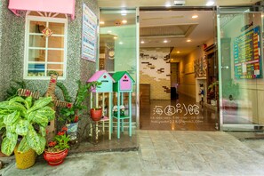 A hotel entrance with a glass door, potted plants, and a sign with contact information. - Hai Yuan Hotel (Hengchun)