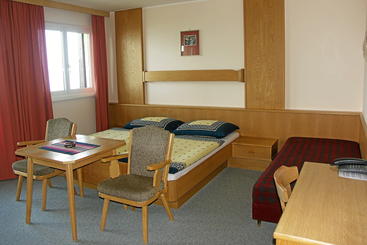 Quarto pequeno com uma cama, uma mesa e uma cadeira.