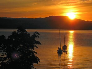 A sunset over a calm lake with two boats anchored, surrounded by hills. - Strandhotel Weyregg (Weyregg am Attersee)