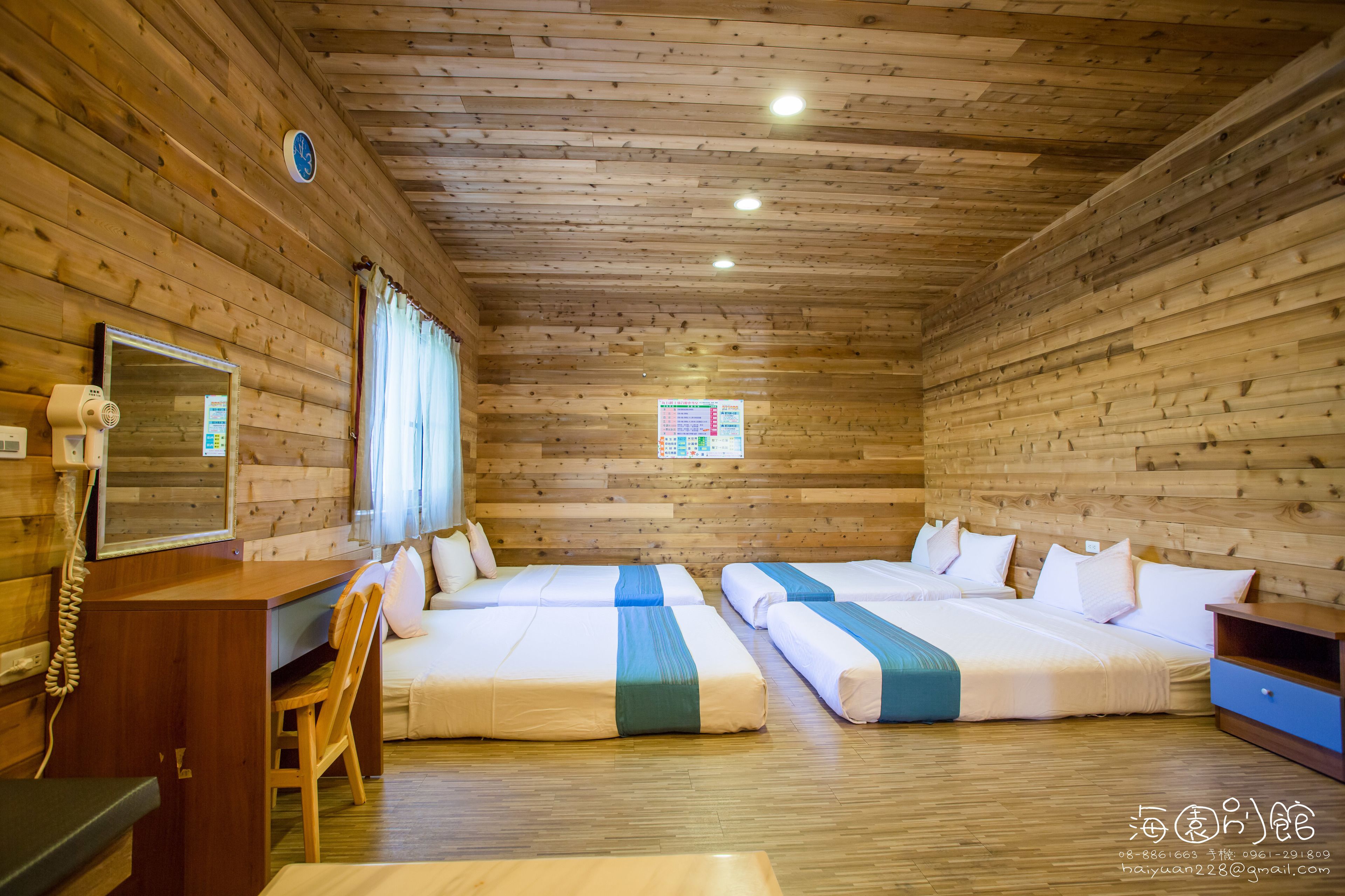 A wooden cabin-style room with four beds, a desk, a chair, and a clock on the wall.