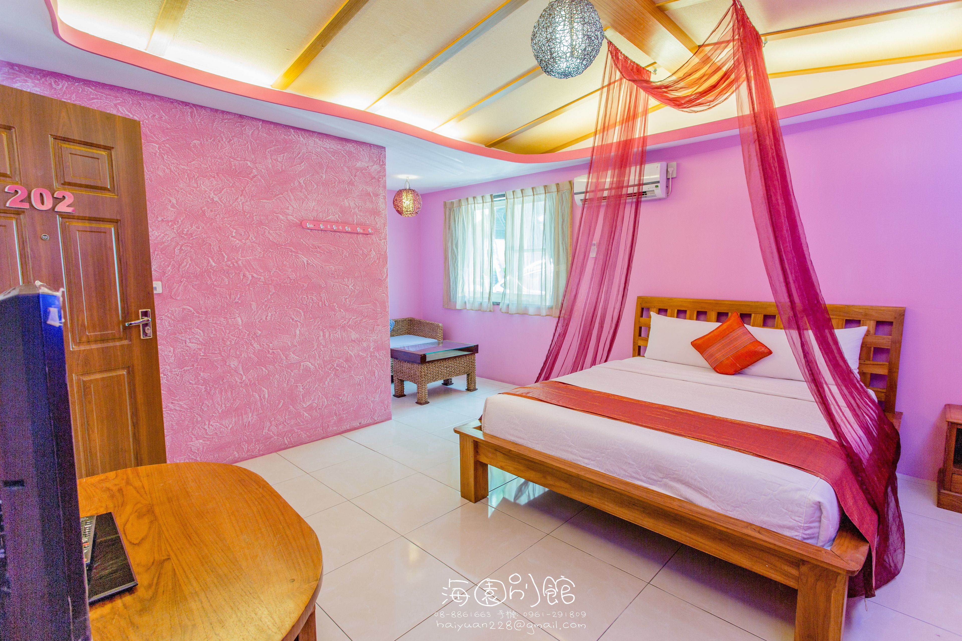 A room with a bed, a wooden door, a chair, a small table, and a window with curtains.