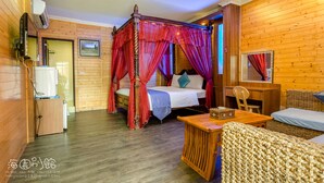 A wooden room with a four-poster bed, a wooden desk, a wicker chair, and a small table with a basket. - Hai Yuan Hotel 2 (Hengchun)