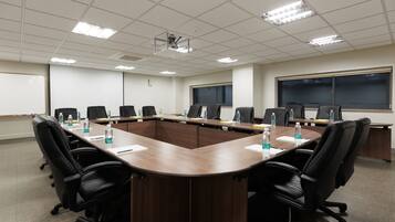 A conference room with a long table, black chairs, water bottles, and a projector screen.