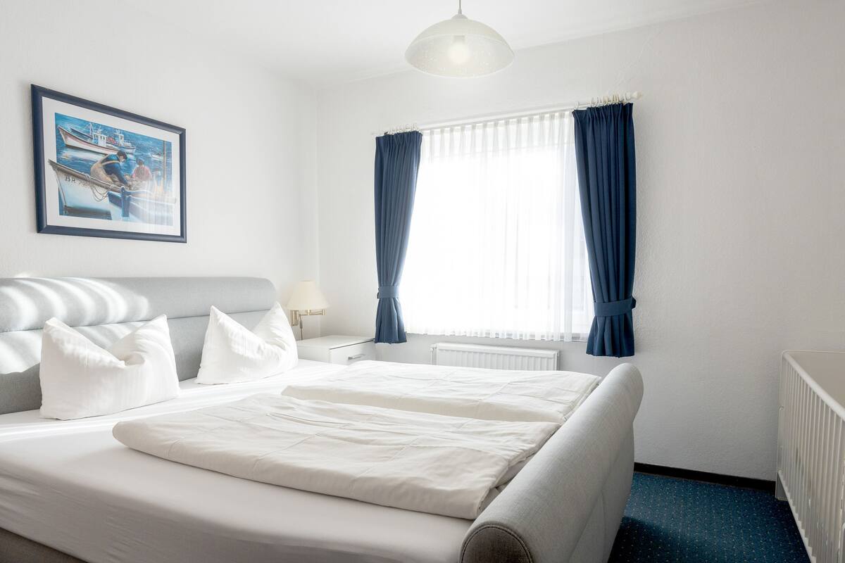 A neatly made bed with white linens, a headboard, and a bedside table with a lamp.