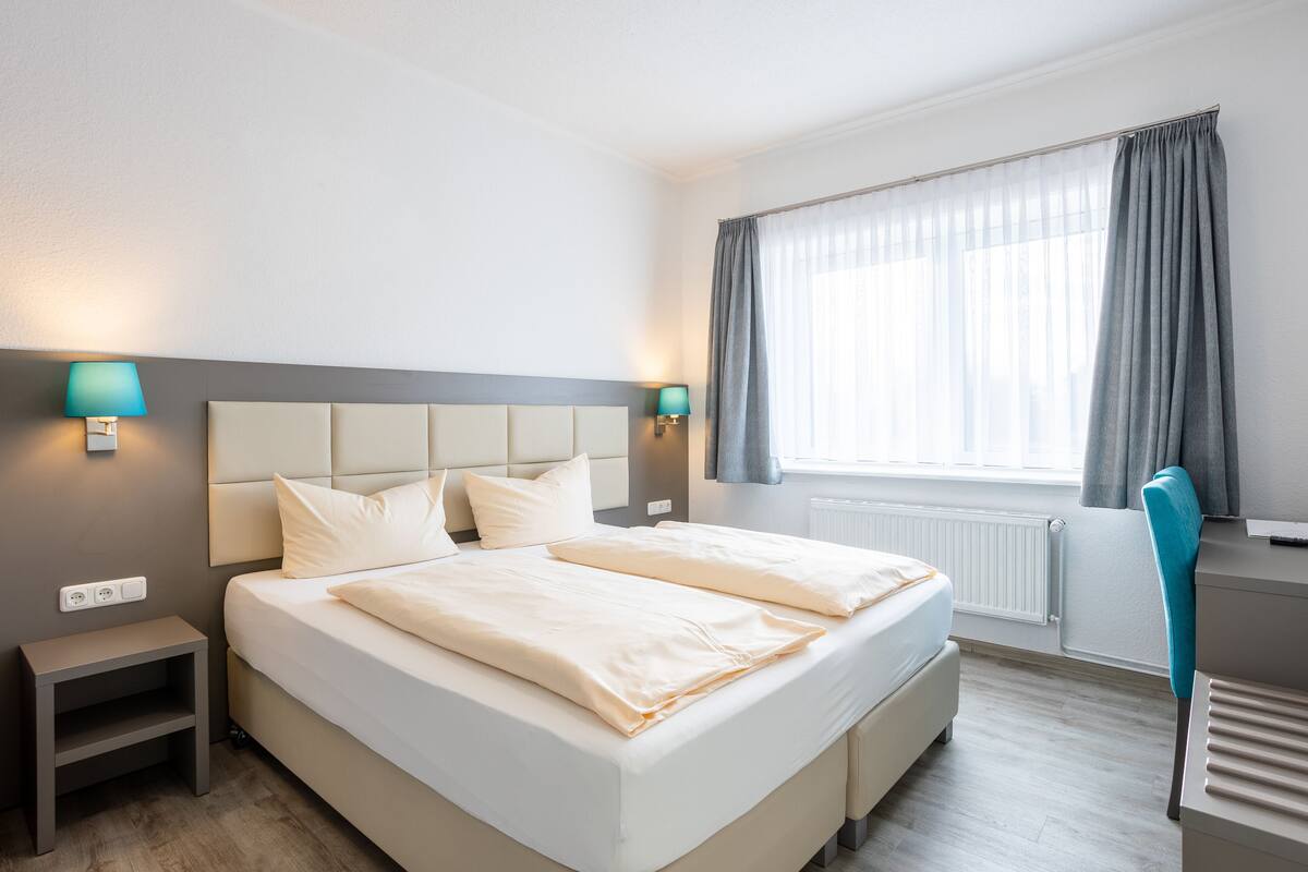 A neatly arranged hotel room with a large bed, bedside lamps, a desk, and a window with curtains.