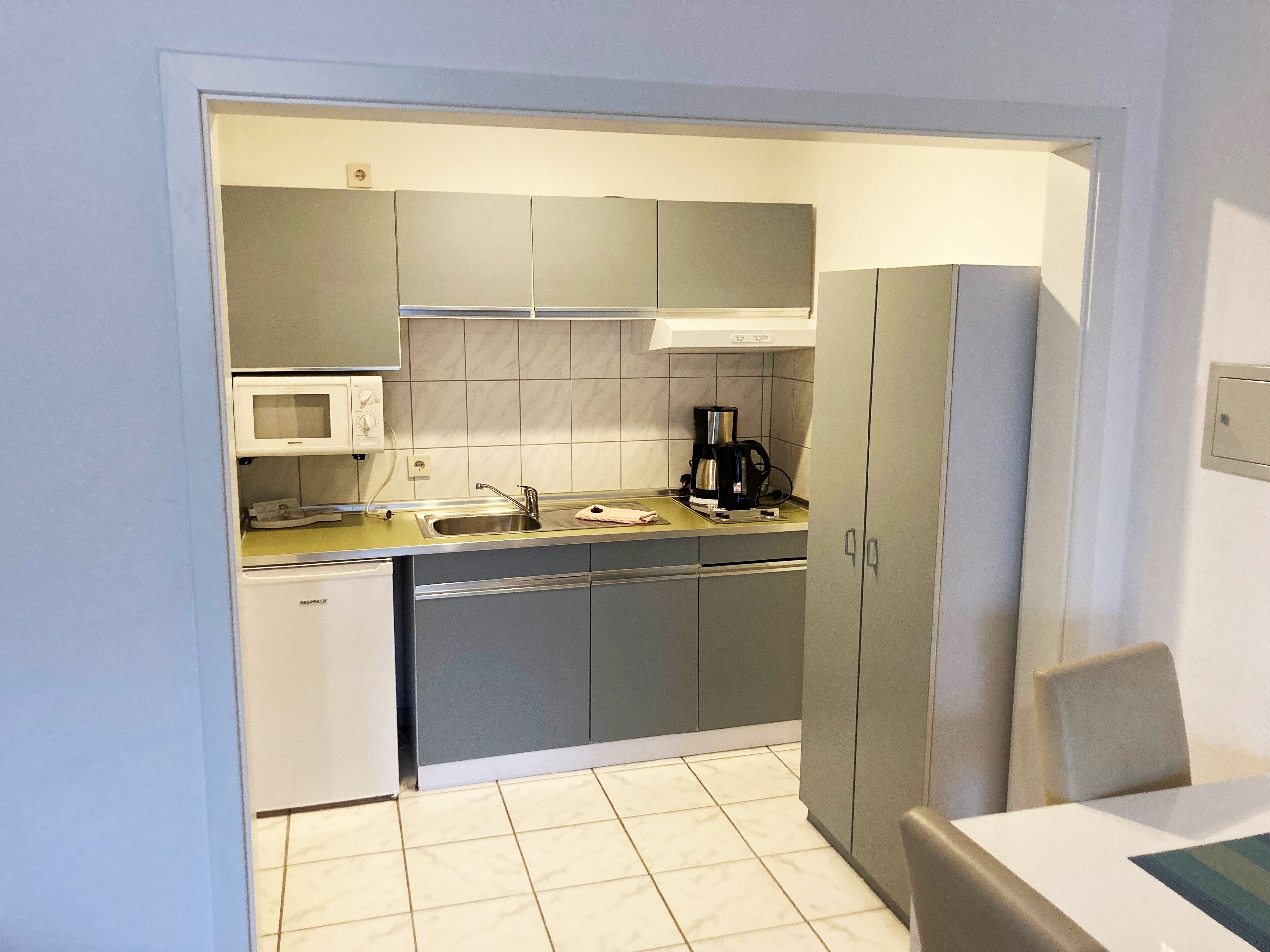 A compact kitchen with grey cabinets, a microwave, a coffee maker, and a sink.