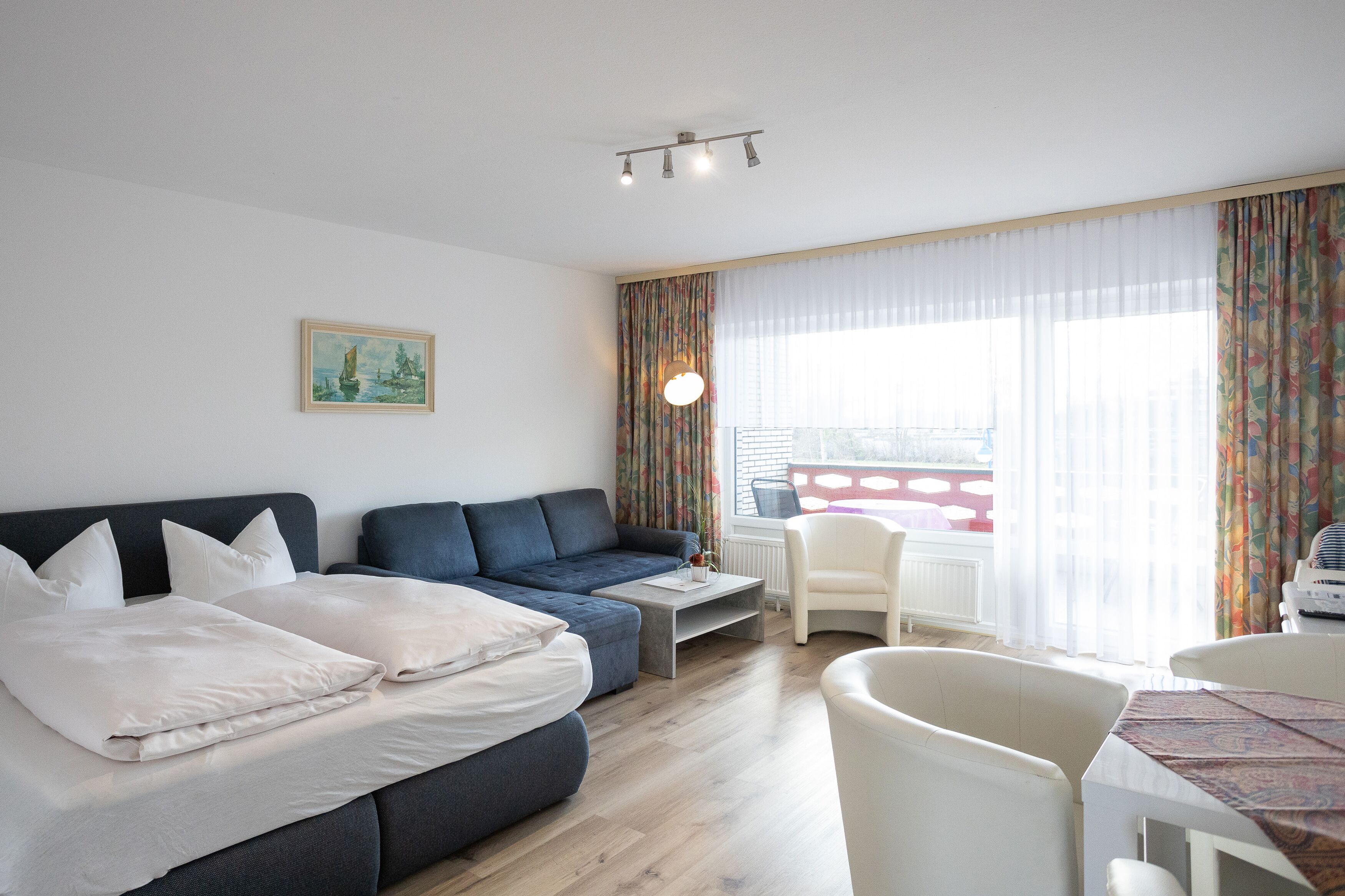 Una habitación de hotel moderna con sofá cama, una mesita, una silla y vistas a la ciudad a través de amplias ventanas.