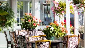 A dining area with wooden chairs and tables, surrounded by potted plants and flowers. - Familien- & Aparthotel Strandhof (Butjadingen)