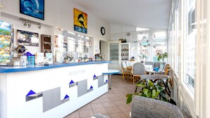 A reception area with a counter, seating, and a view of the street. - Familien- & Aparthotel Strandhof (Butjadingen)