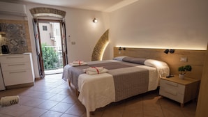 A bedroom with a bed, bedside tables, a nightstand, a small potted plant, and a view of the outside balcony. - B&B La Suite (Milazzo)