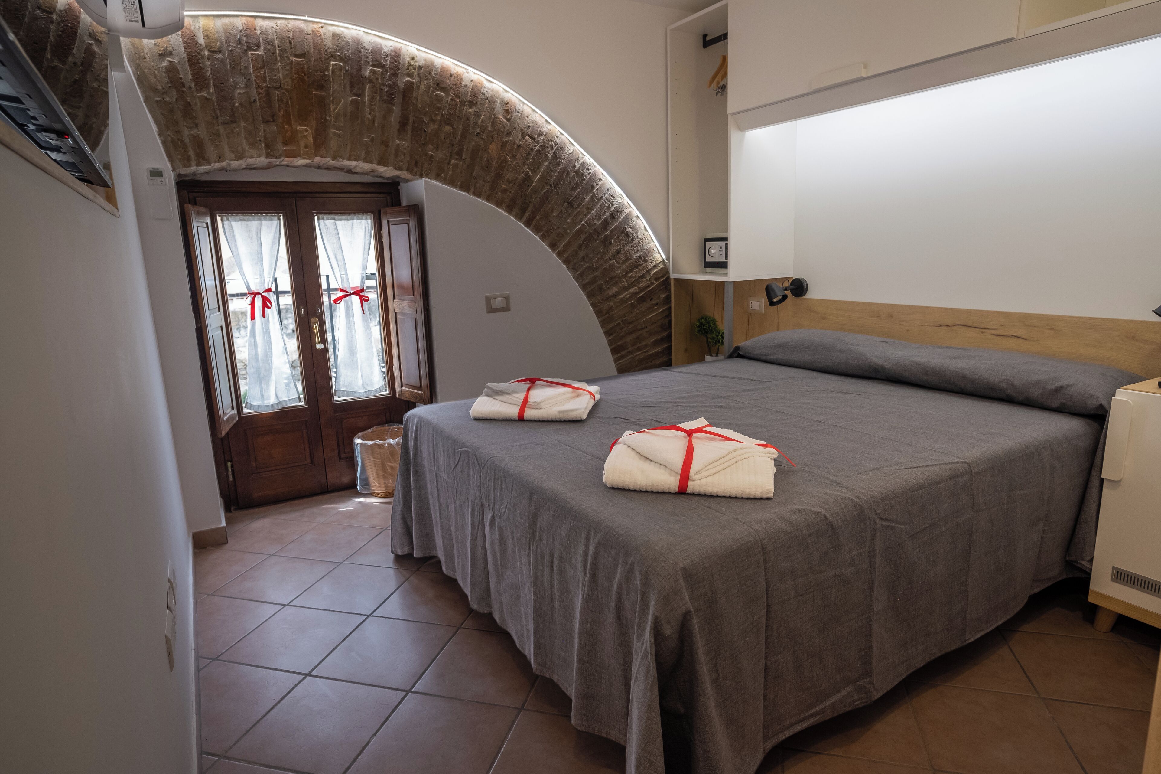 A bedroom with a curved stone archway, a bed with gray bedding, and a bedside table.