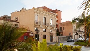 A multi-story building with balconies, a sign for 'La Suite Bed & Breakfast', and a street with cars and palm trees. - B&B La Suite (Milazzo)