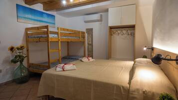 A bedroom with bunk beds, a bed with a beige cover, a wall-mounted wardrobe, a hanging coat rack, and a painting of a beach scene.