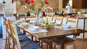 A modern kitchen with wooden furniture, a dining table set for four, and a vase with red flowers. - B&B La Suite (Milazzo)