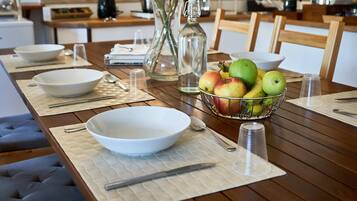 Une table à manger dressée avec des bols, des cuillères, un couteau, une bouteille en verre et un saladier rempli de fruits.