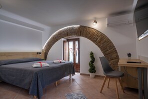 A bedroom with a bed, a desk, a chair, a potted plant, and an arched doorway. - B&B La Suite (Milazzo)