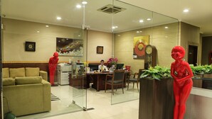 A hotel lobby with a reception desk, a sofa, a dining area, and a large mirror reflecting the space. - Hotel 55 (Jakarta)
