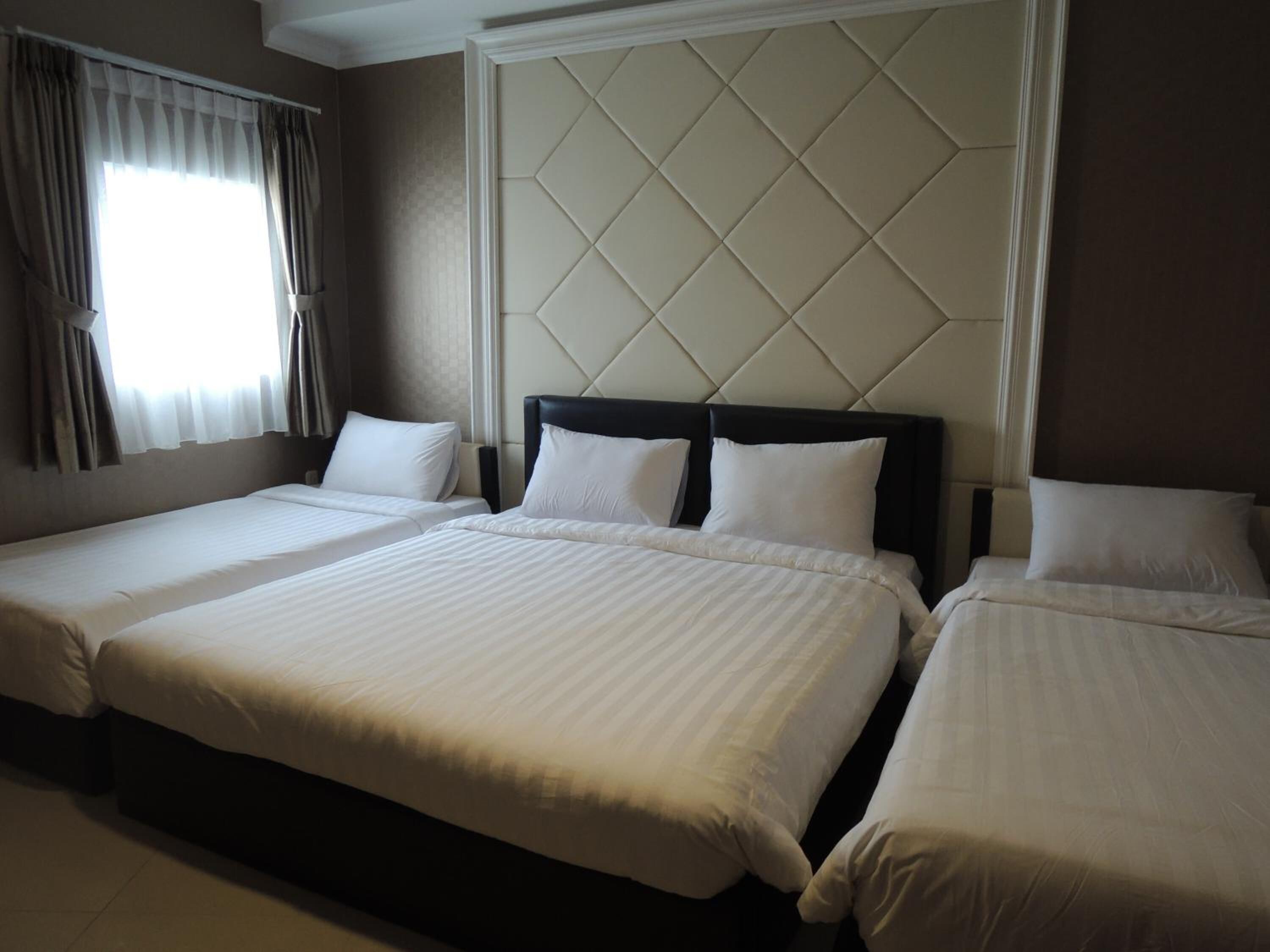 A hotel room with three single beds, a large window with curtains, and a padded headboard.