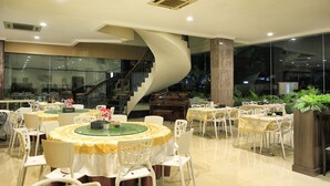 A modern dining area with round tables, white chairs, and a spiral staircase. - Hotel 55 (Jakarta)