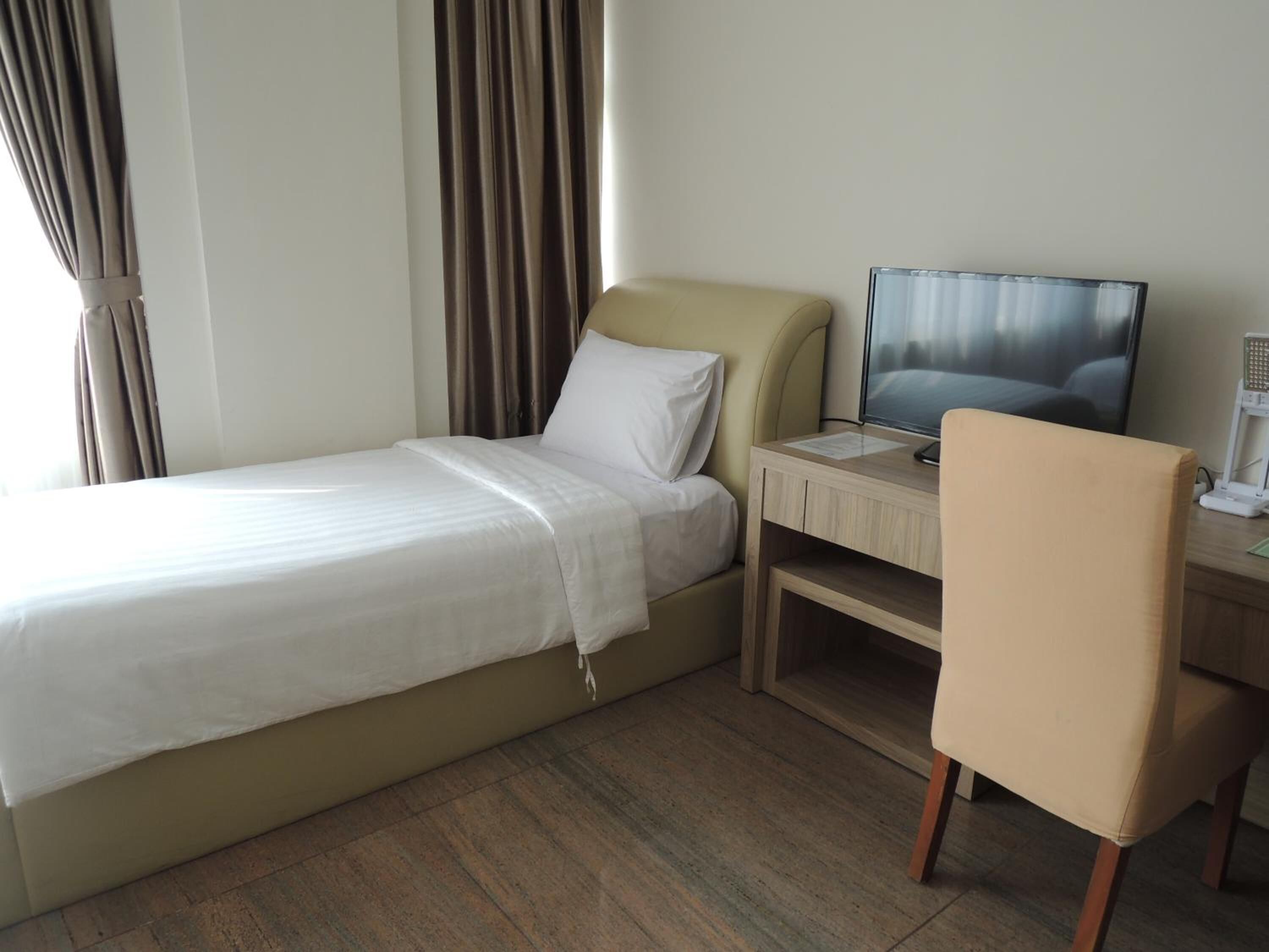 Ein Hotelzimmer mit einem Einzelbett, einem Schreibtisch mit Computer, einem Stuhl und einem Fernseher.