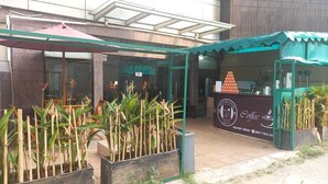 A coffee shop with outdoor seating, a delivery order sign, and a green awning. - Hotel 55 (Jakarta)