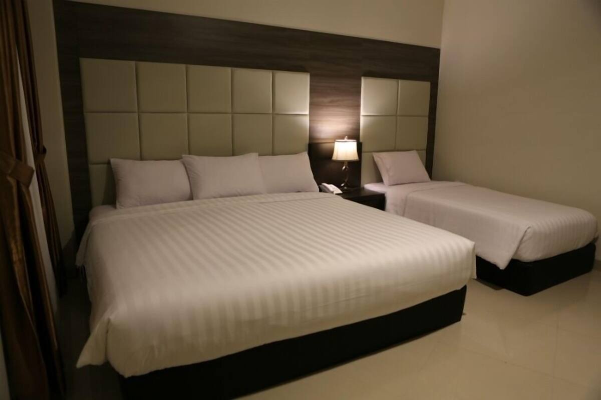 Una habitación de hotel con una cama grande, una cama más pequeña y una mesita de noche con una lámpara.