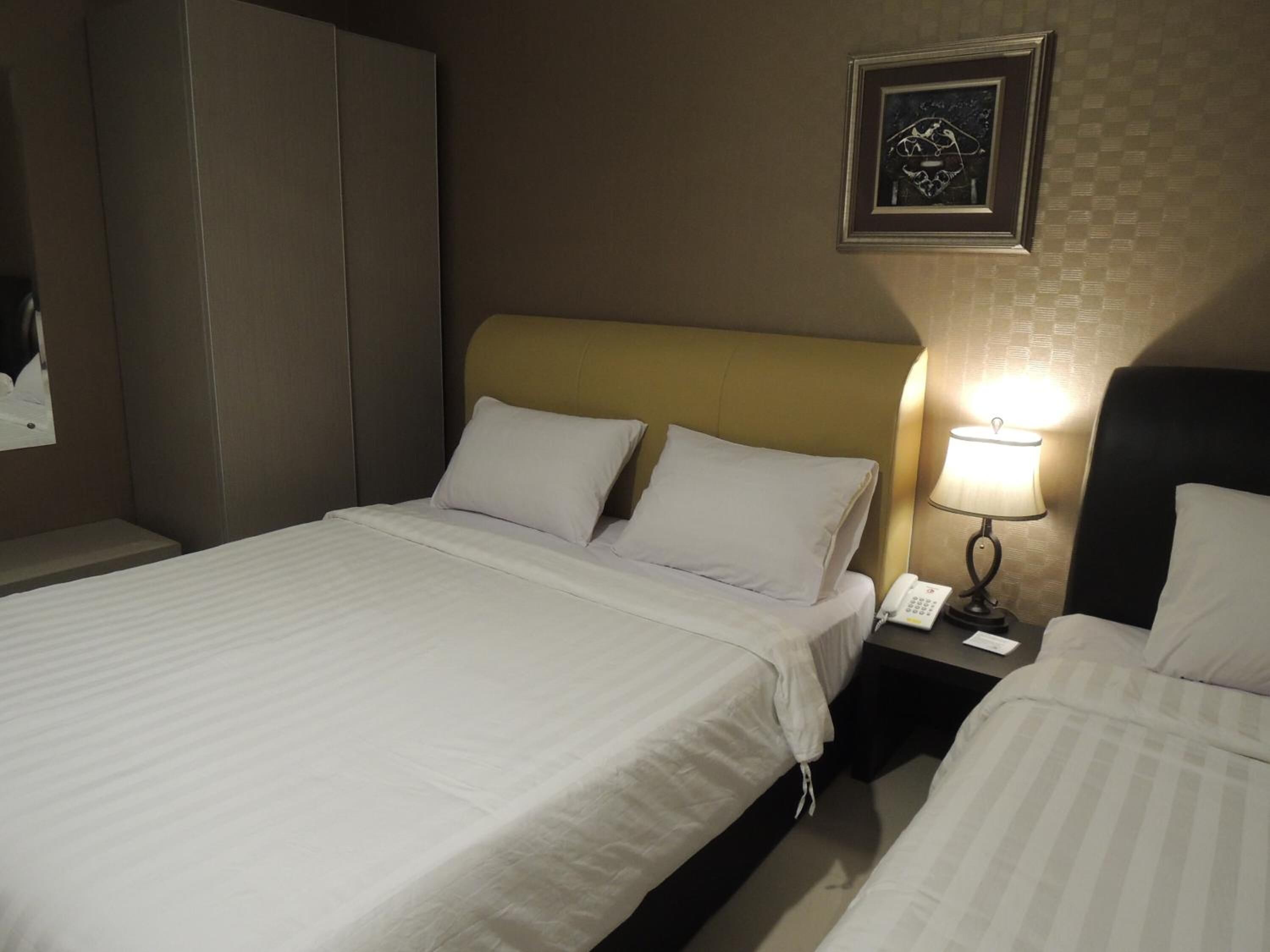 A hotel room with two beds, a nightstand with a lamp, and a framed picture on the wall.