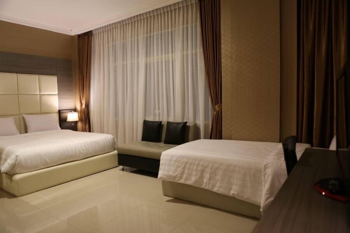 Habitación de hotel con dos camas, un escritorio, una lámpara y un ventanal grande con cortinas.