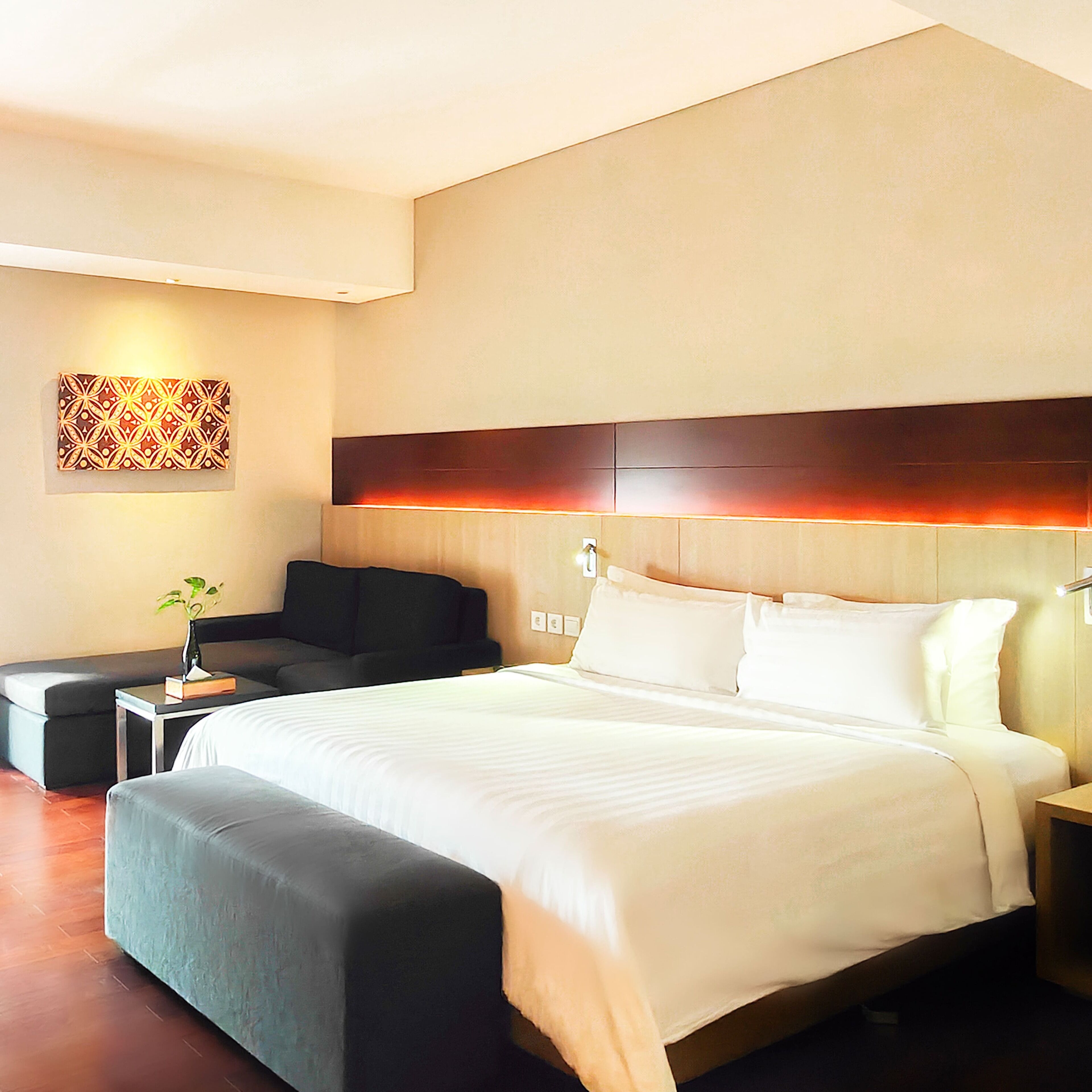 Una habitación de hotel moderna con una cama grande, una mesita de noche, un sofá y un elemento decorativo en la pared.