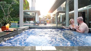 Una pareja en un jacuzzi con vista a un edificio moderno y un área de piscina.