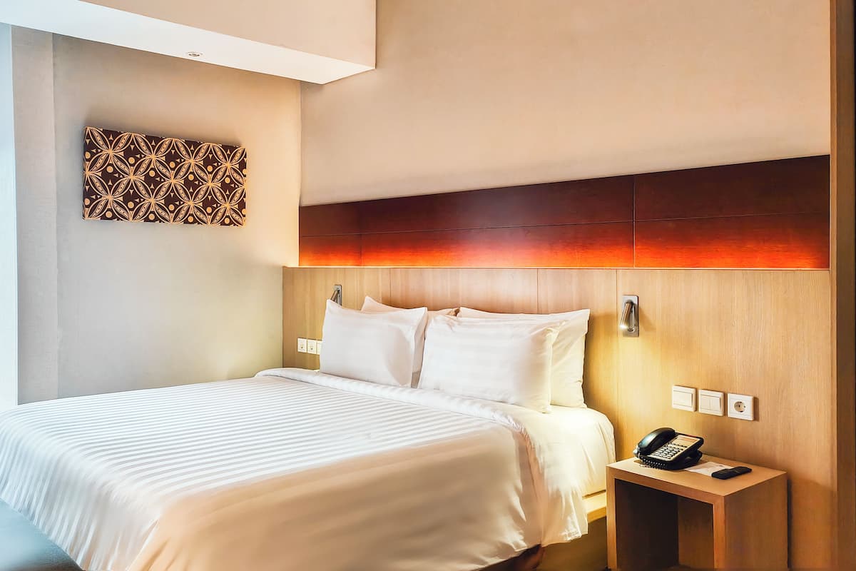 A hotel room with a large bed, a bedside table with a phone, and a city view through the window.