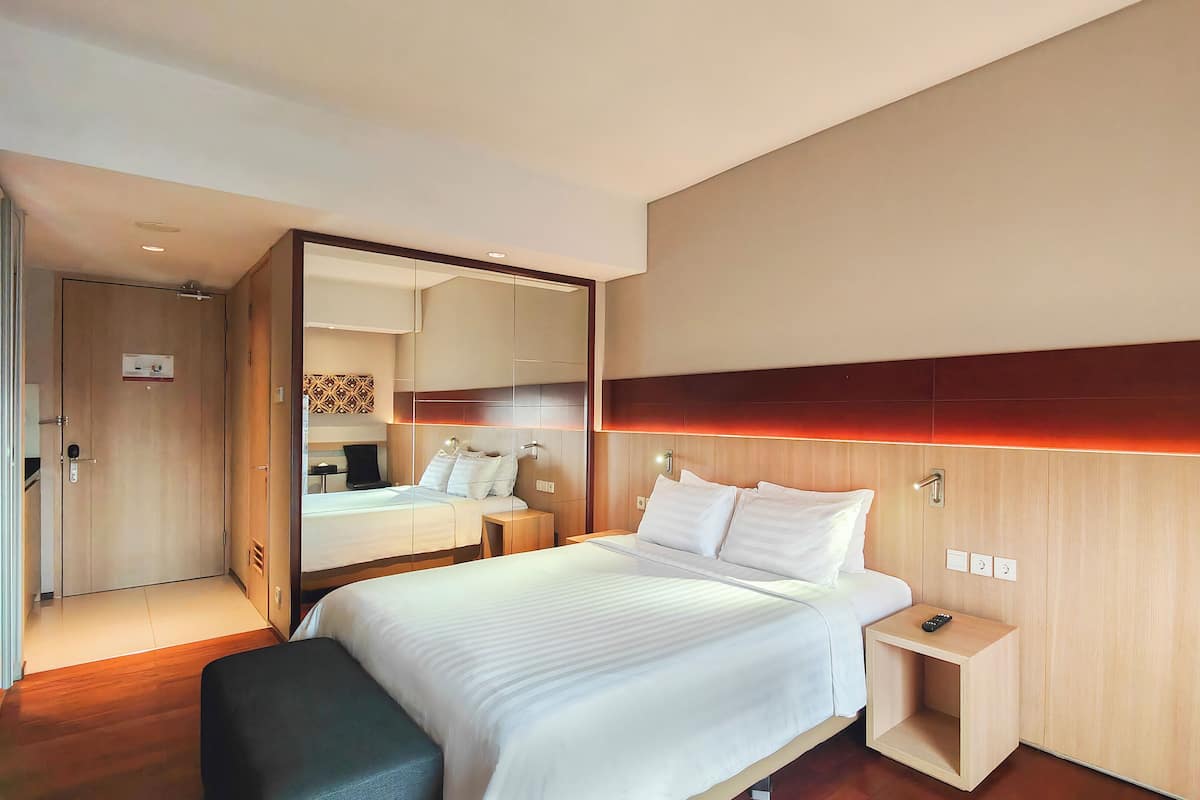 A modern hotel room with a large bed, bedside tables, a mirror, and a wooden headboard.