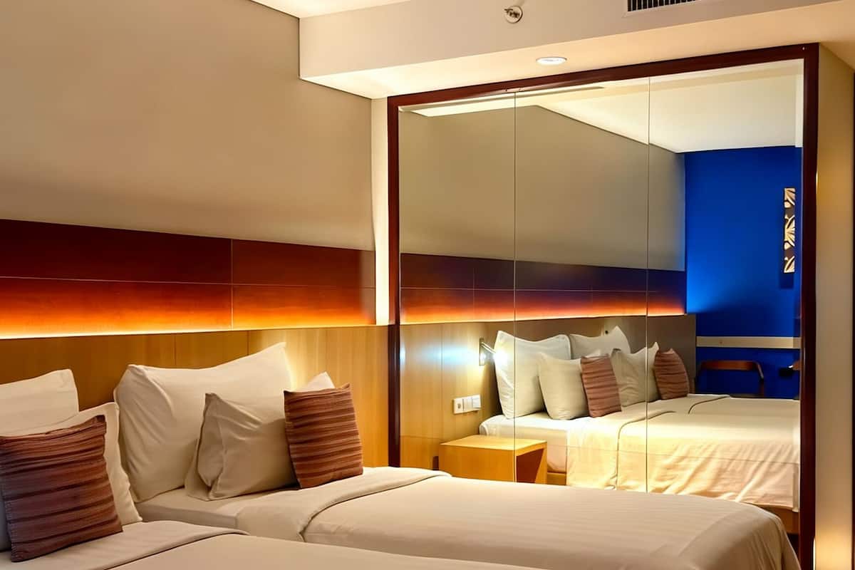 A hotel room with two beds, a large mirror, and a modern design.