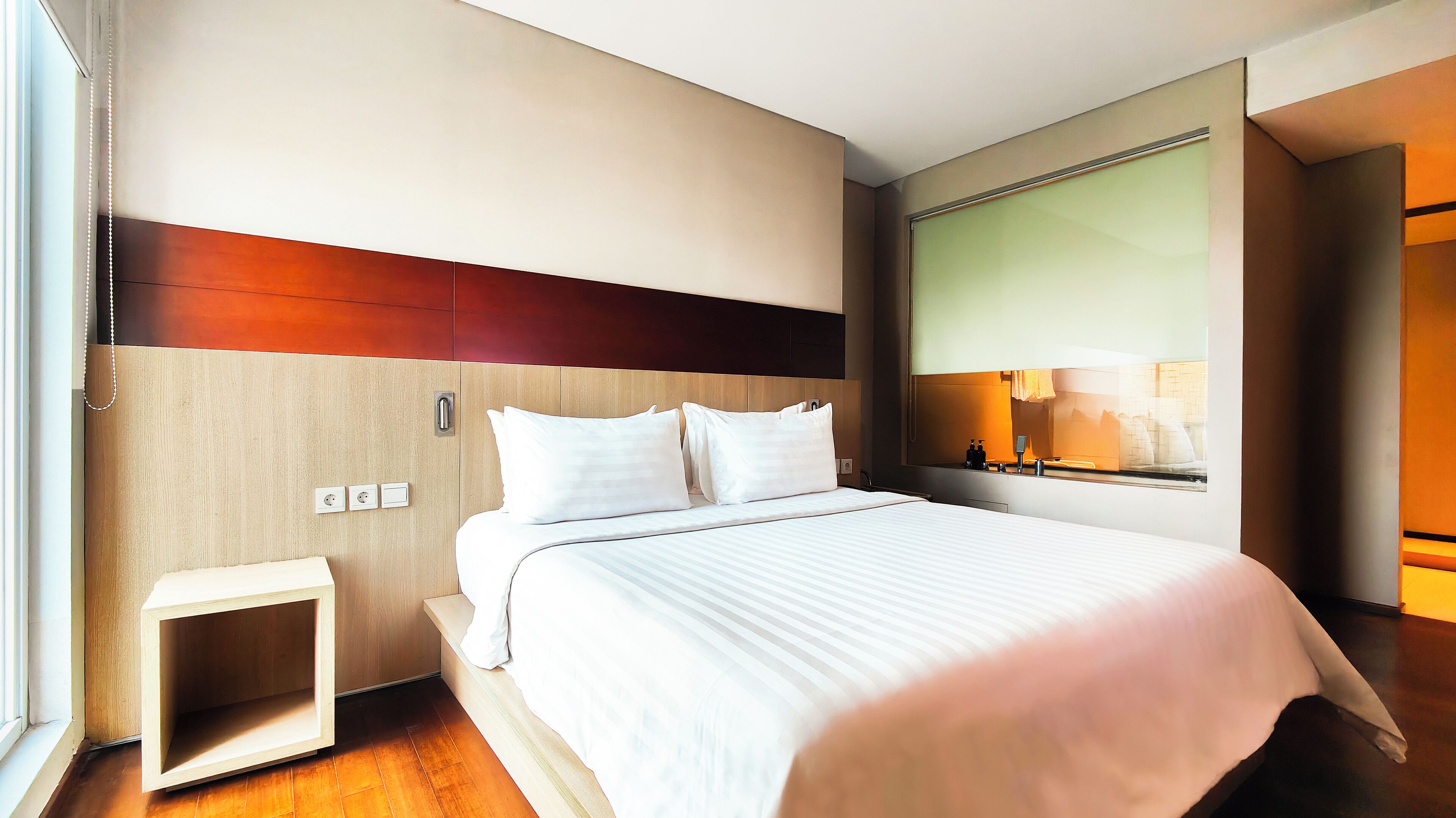 Een moderne hotelkamer met een groot bed, een houten hoofdeinde, een nachtkastje en een grote spiegel.