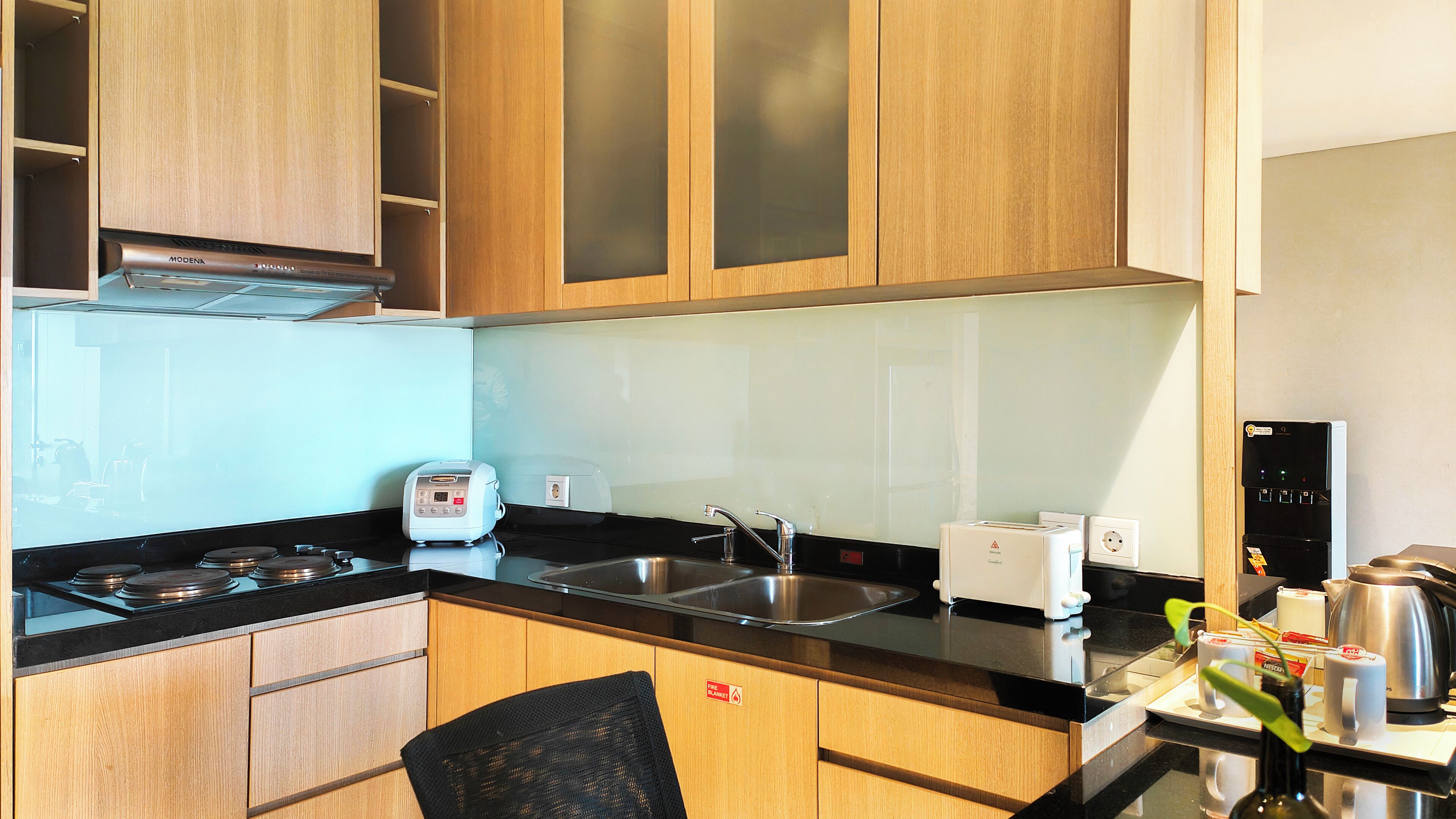 Cocina compacta con armarios de madera, estufa a gas, lavadero, tostadora y dispensador de agua.