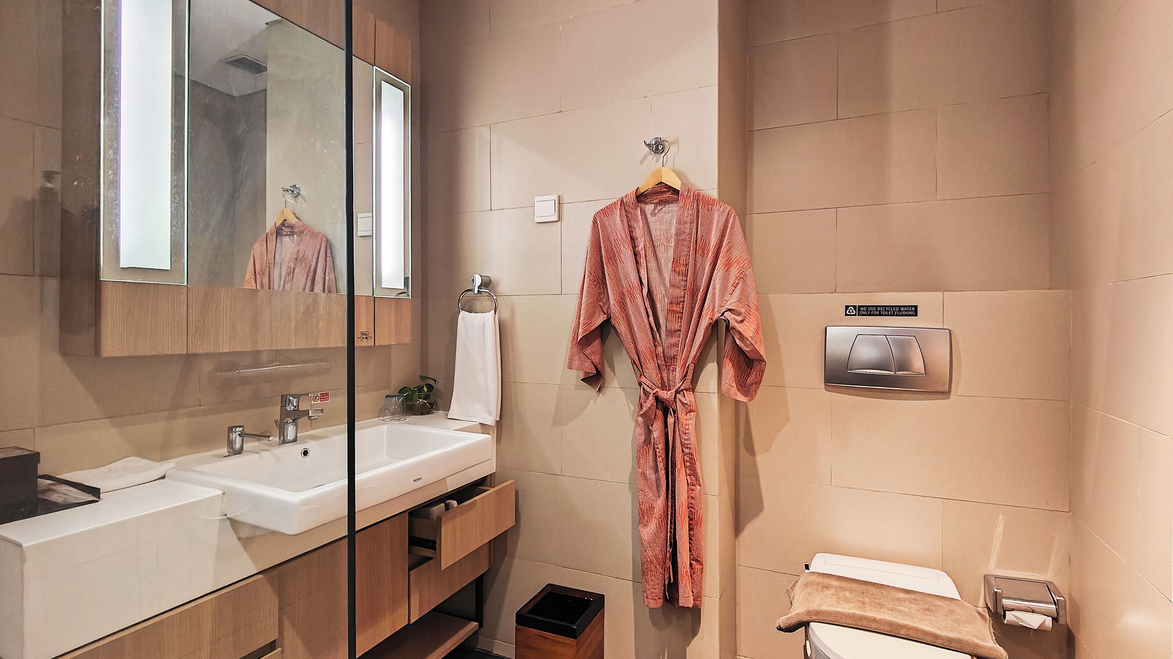A modern bathroom with a large mirror, two sinks, a towel rack, and a toilet.